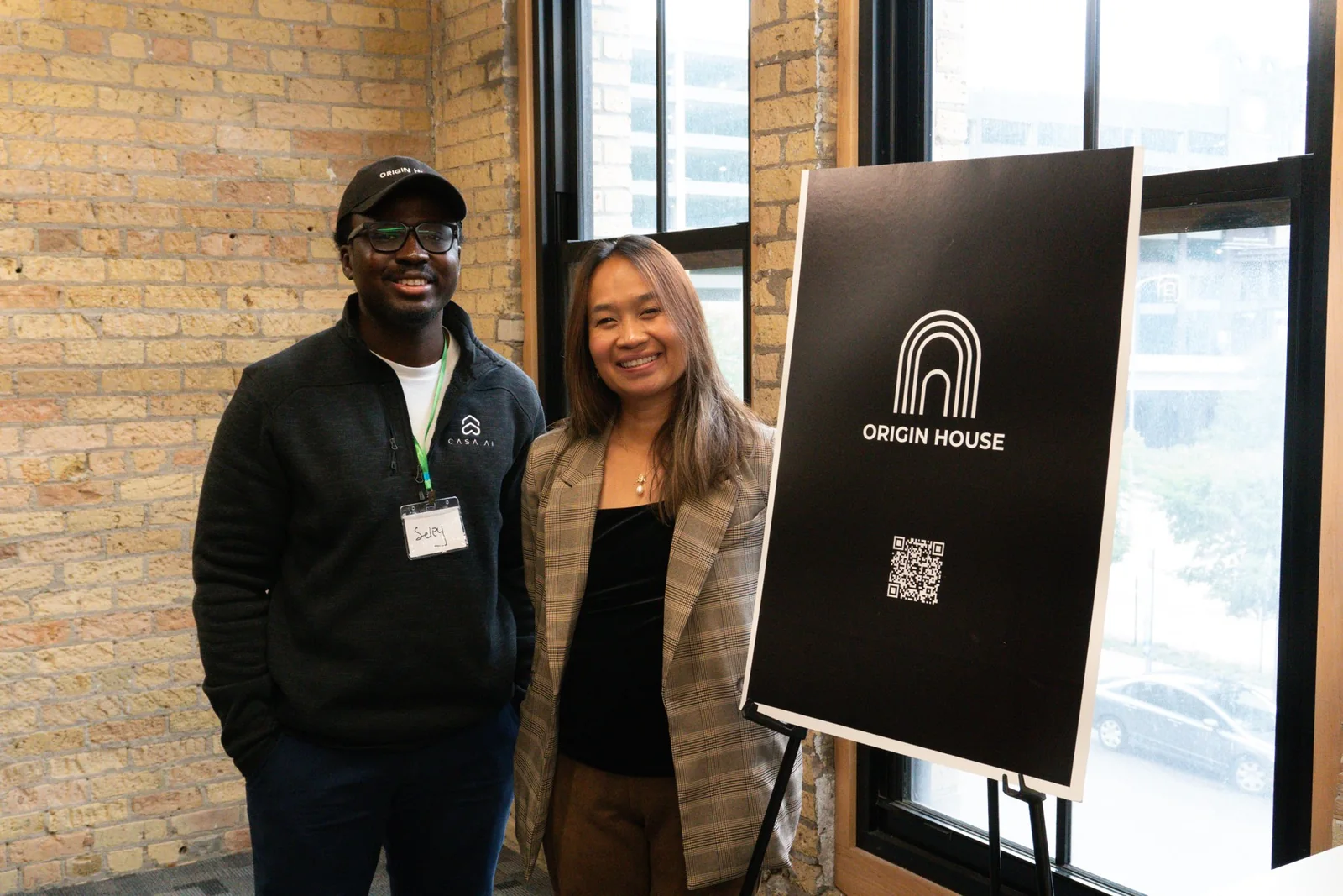 Two opening-day attendees beside an Origin House sign inside the house