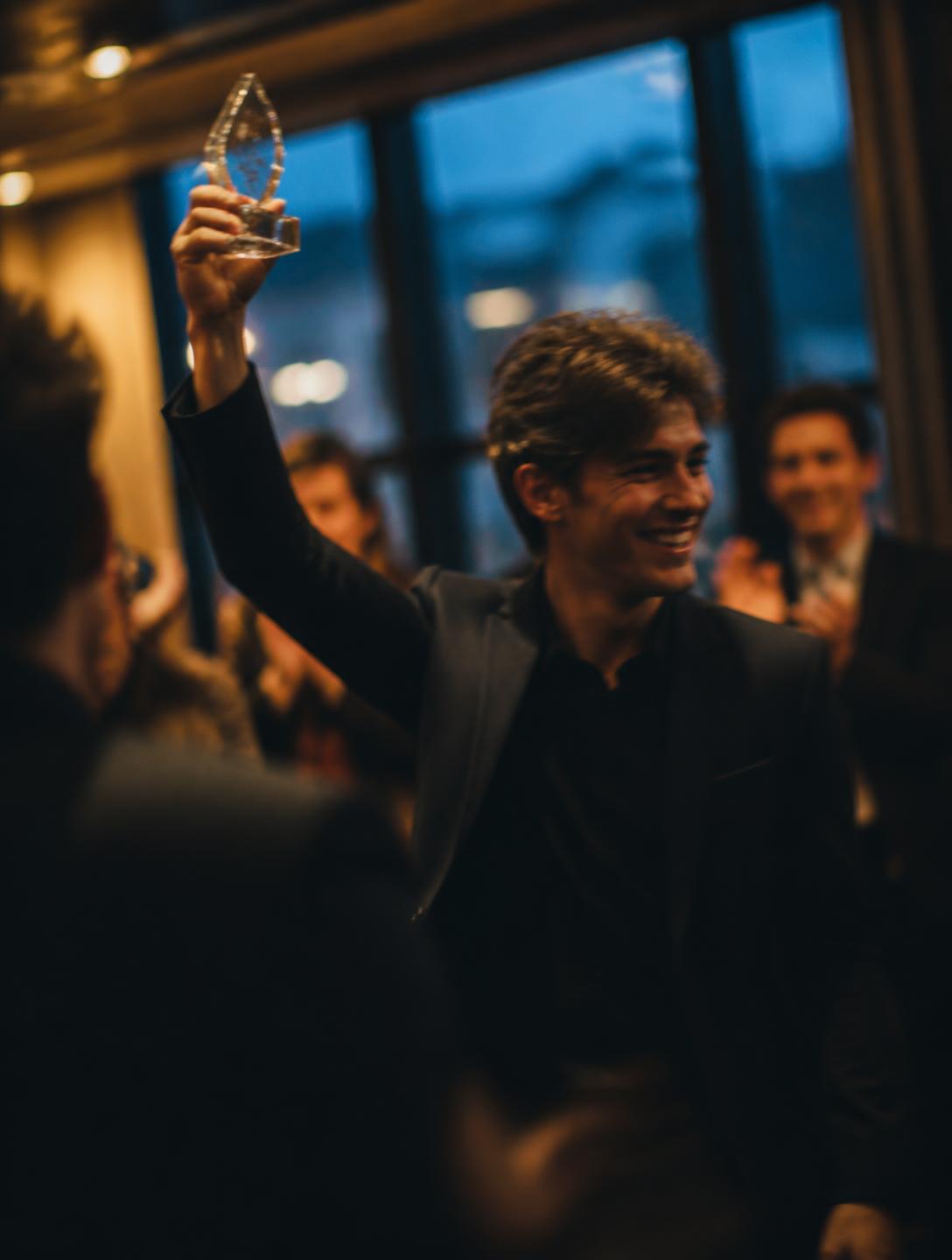 Founders reaching for a glass award held up in a dim room at dusk